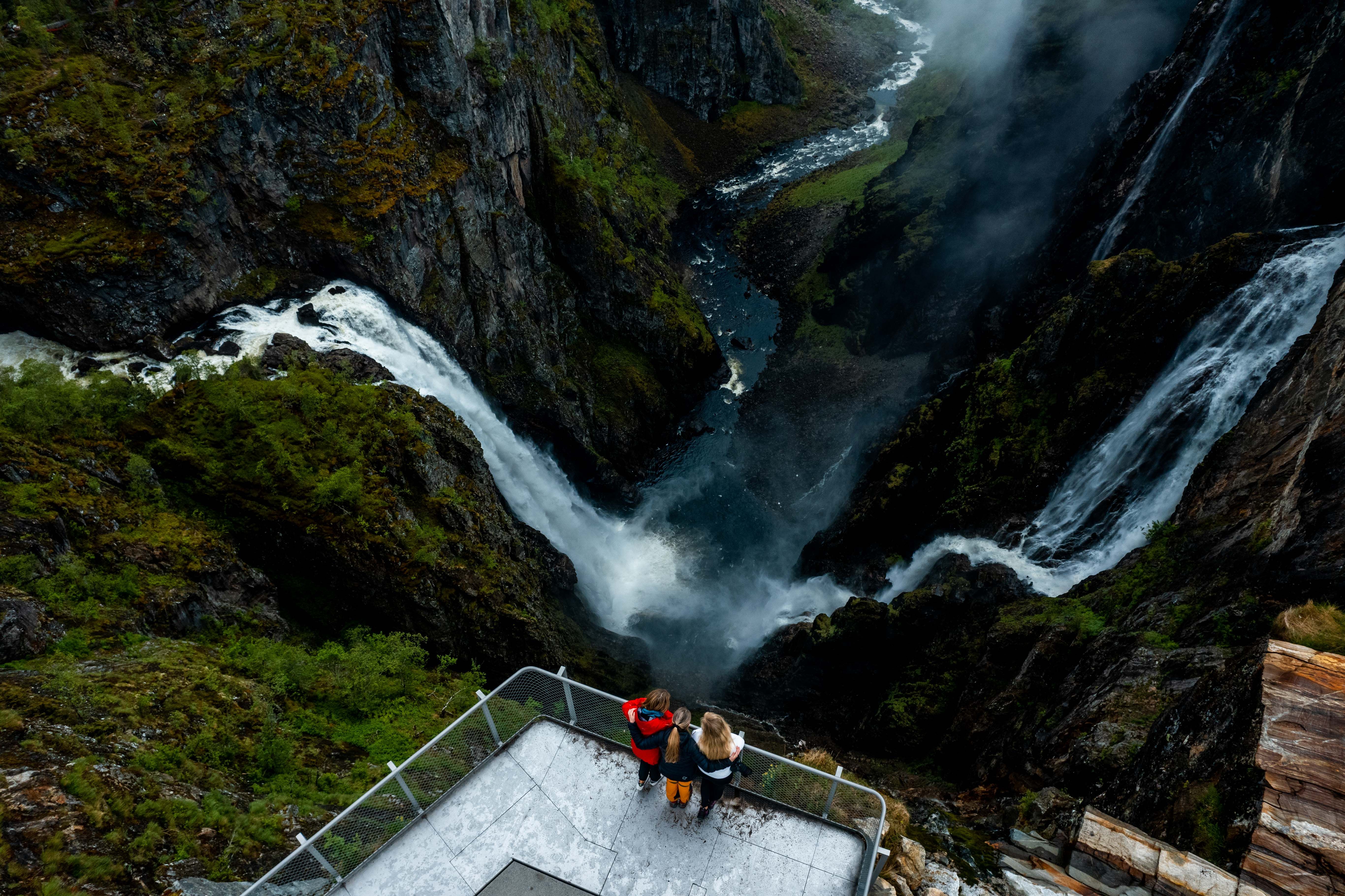 Et dronebilde der du ser tre personer på utsiktsplattformen over fossen.