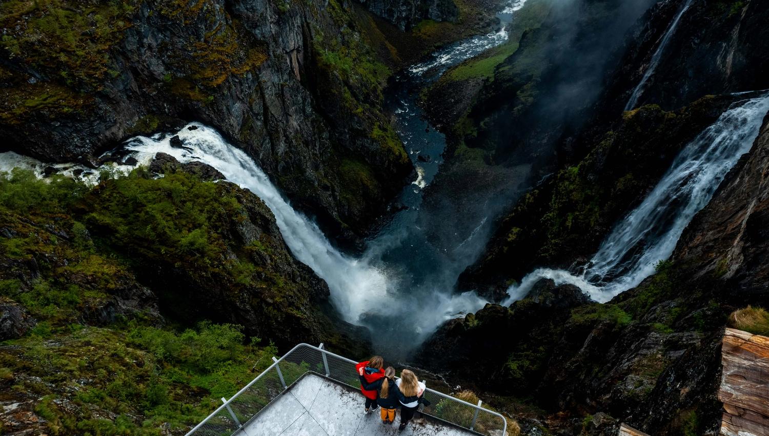 Et dronebilde der du ser tre personer på utsiktsplattformen over fossen.