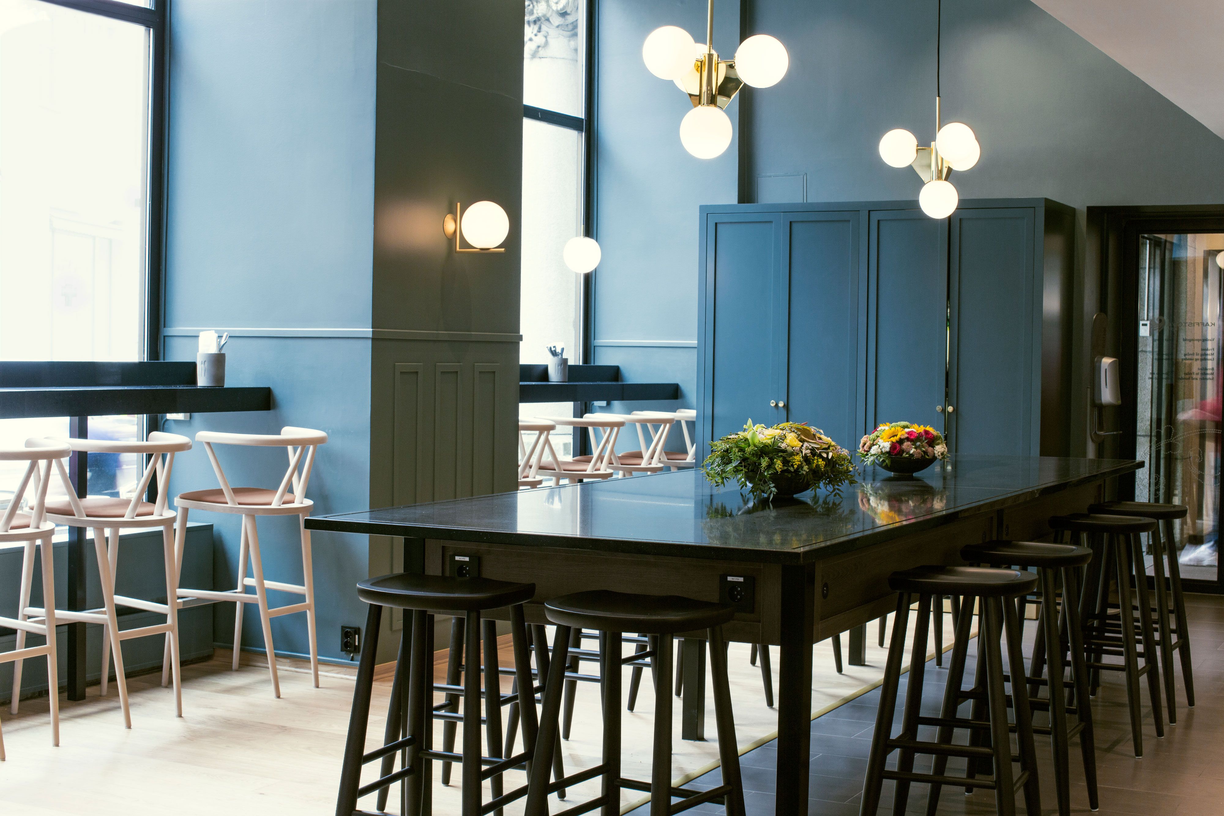 Sort langbord med krakker, blå vegger og runde taklamper.