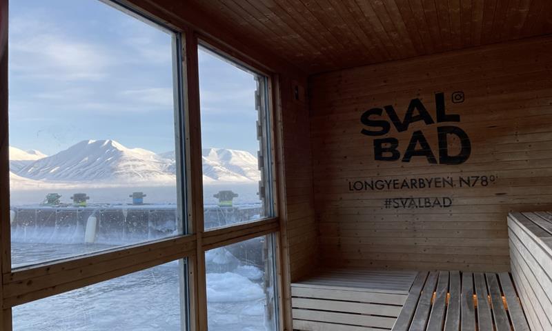 Utsikten mot fjellandskap og en fjord fra innsiden av badstuen