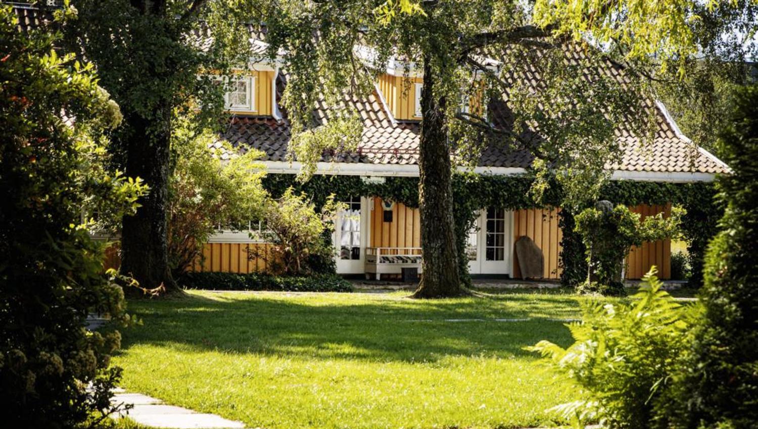 Grønn hage med gult hus i bakgrunnen