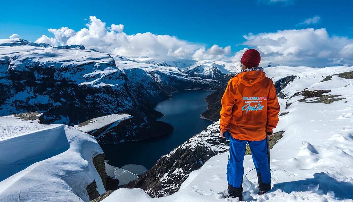 Guide in an orange jacket overlooking the fjord and winter landscape at Trolltunga.