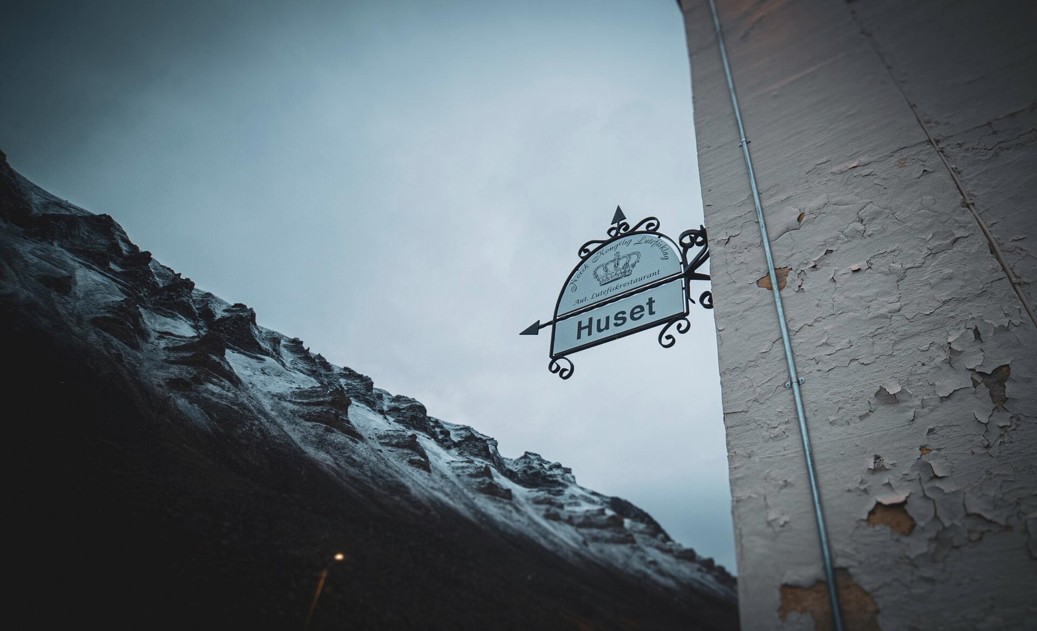 A sign next to the entrance to Huset with mountains in the background