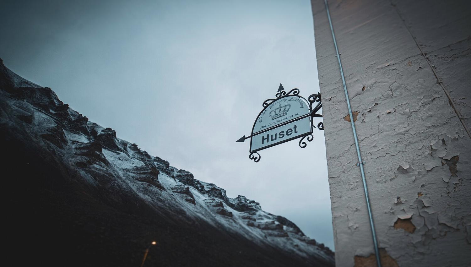 A sign next to the entrance to Huset with mountains in the background