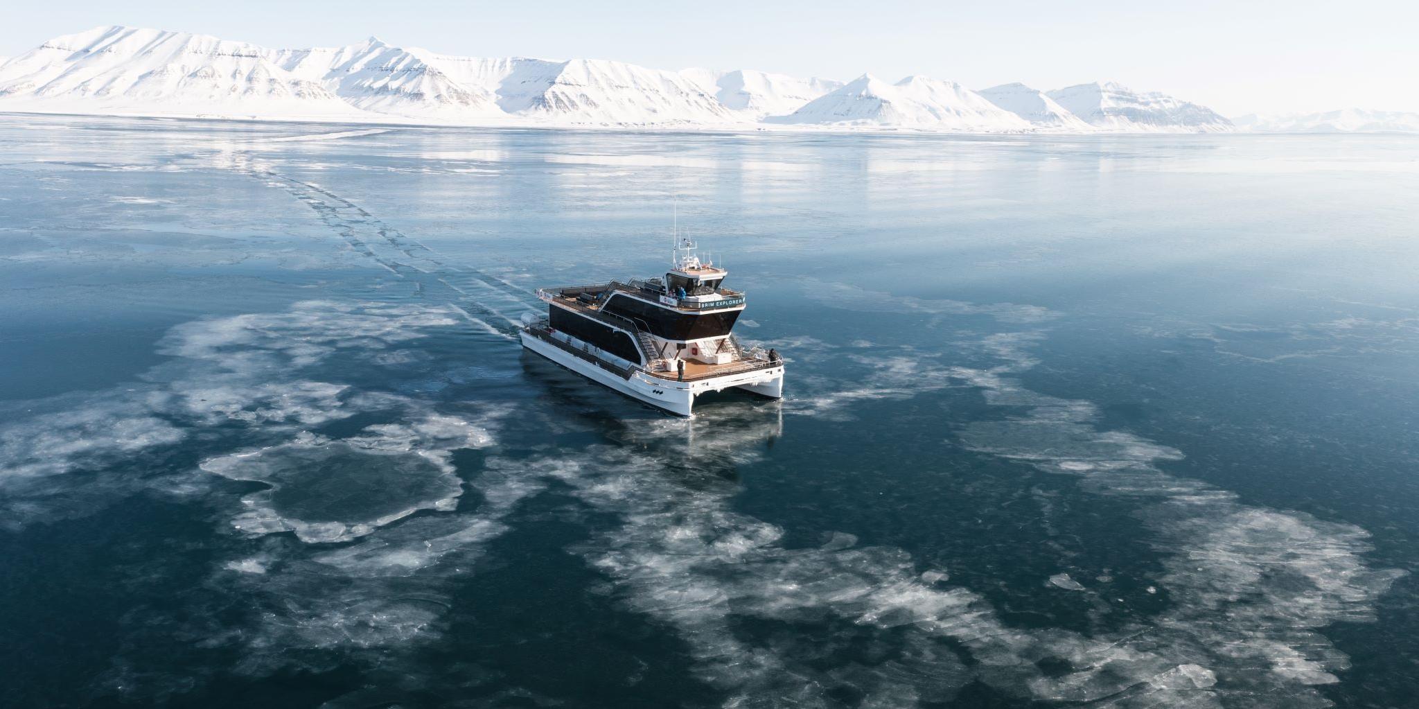 A boat (MS Bard) sailing through thin drift ice on a fjord with mountains in the background