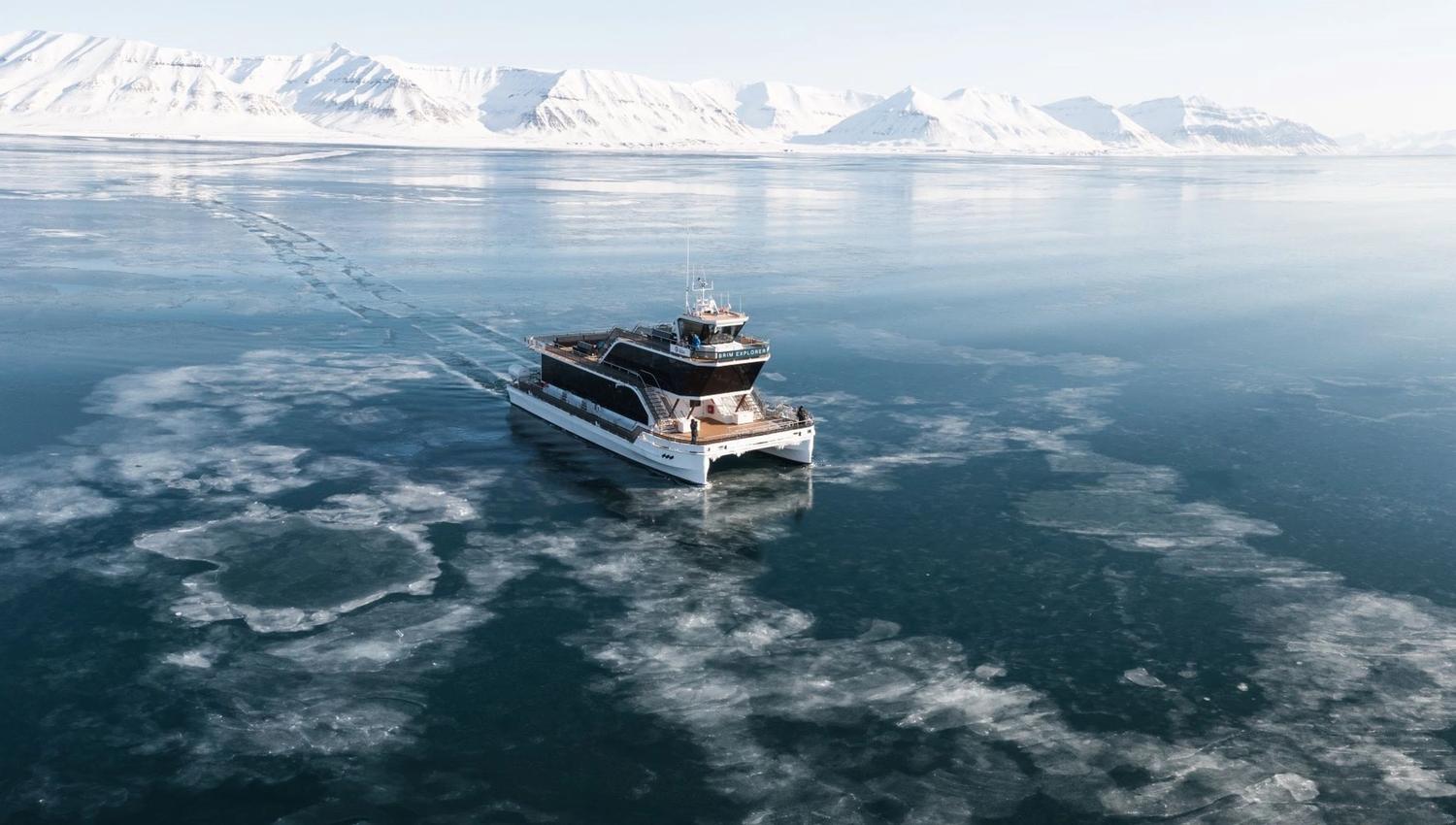 A boat (MS Bard) sailing through thin drift ice on a fjord with mountains in the background