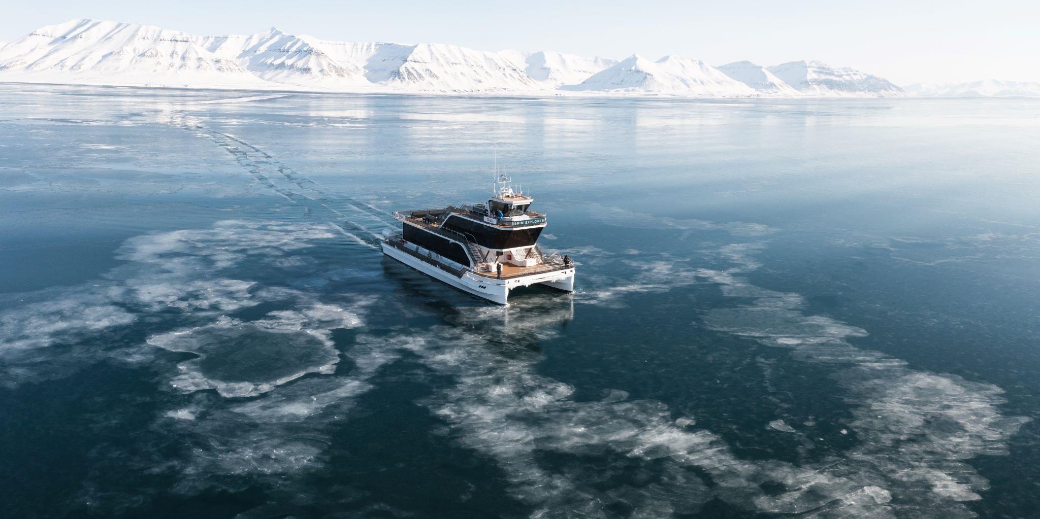 A boat (MS Bard) sailing through thin drift ice on a fjord with mountains in the background