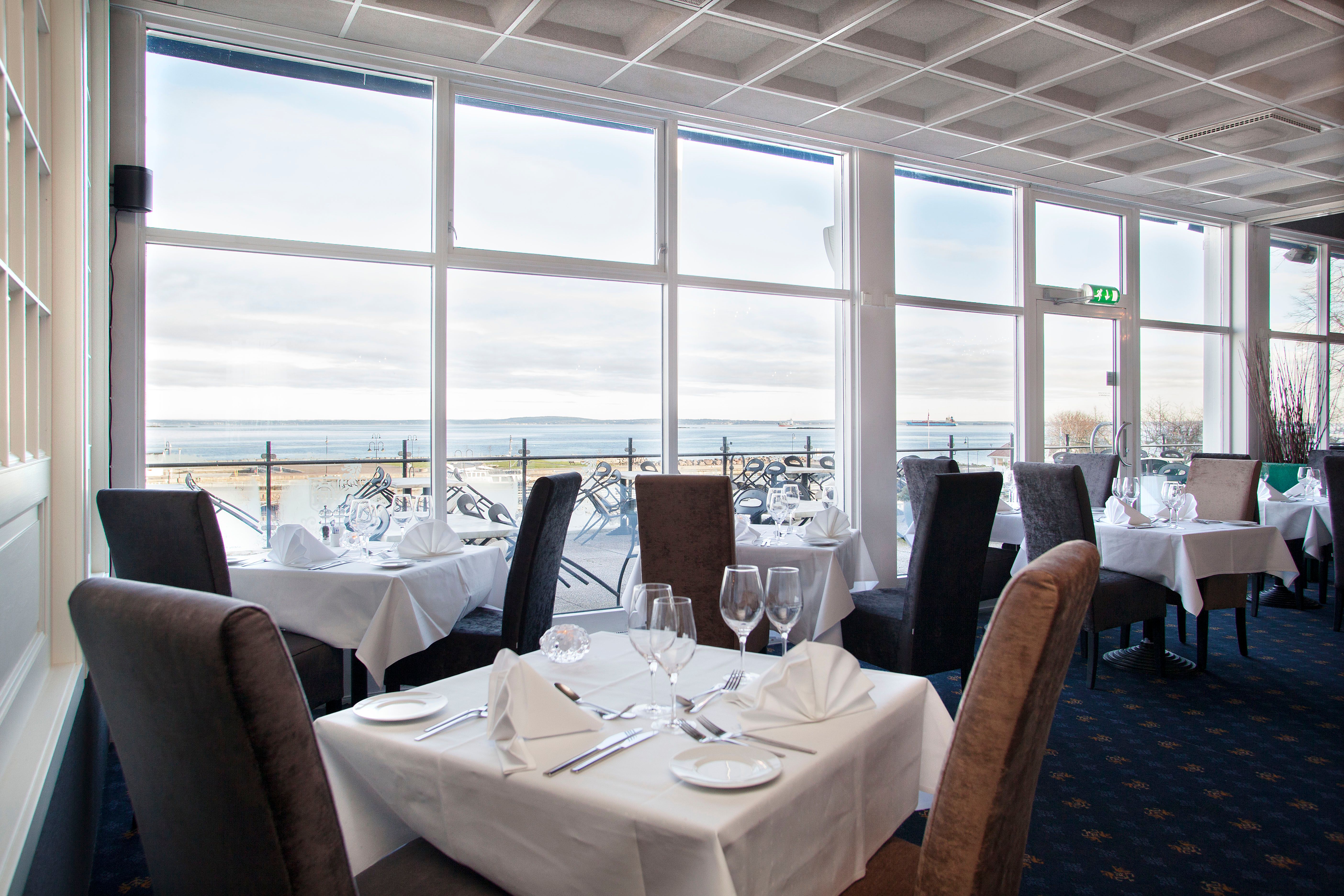 Restaurant med dekket bord og stoler, med utsikt utover vannet