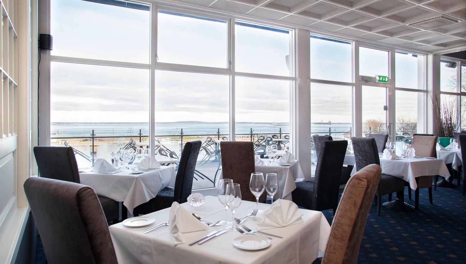 Restaurant med dekket bord og stoler, med utsikt utover vannet