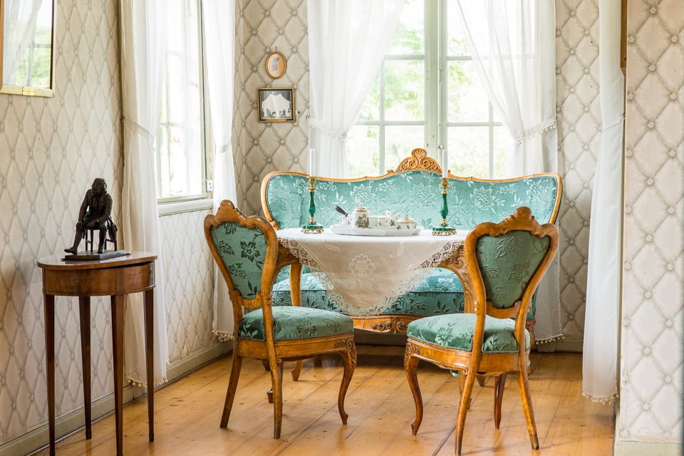 Gammel fasjonabel stue med grønn sofa og grønne stoler, bord med hvit duk og lys.