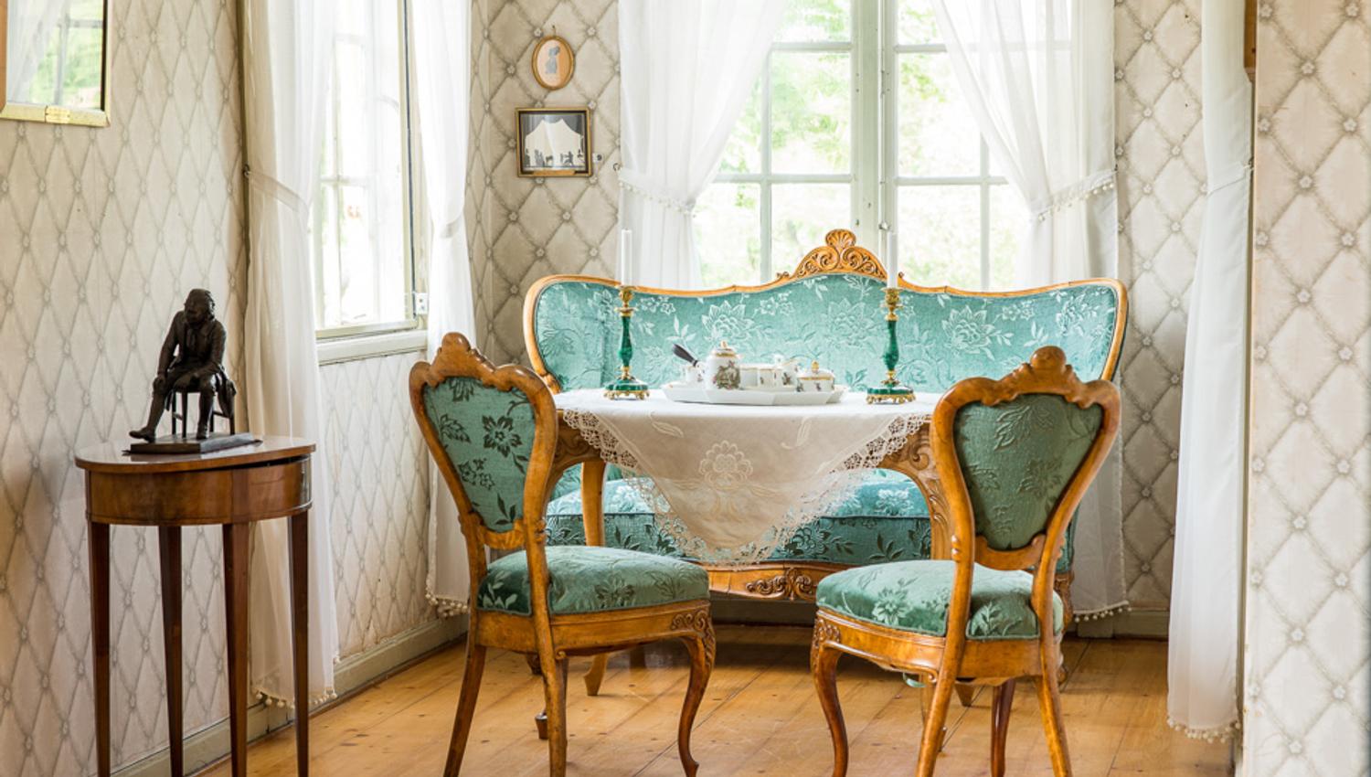 Gammel fasjonabel stue med grønn sofa og grønne stoler, bord med hvit duk og lys.
