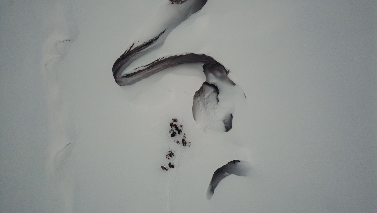 Drone photo of a group of people standing next to a crevasse in a glacier