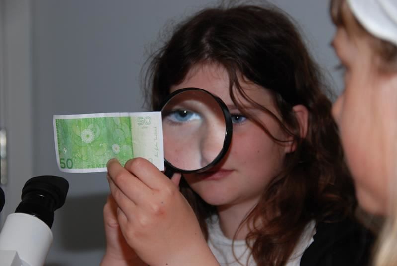 A girl look closer at a 50 kroner note with a magnifying glass