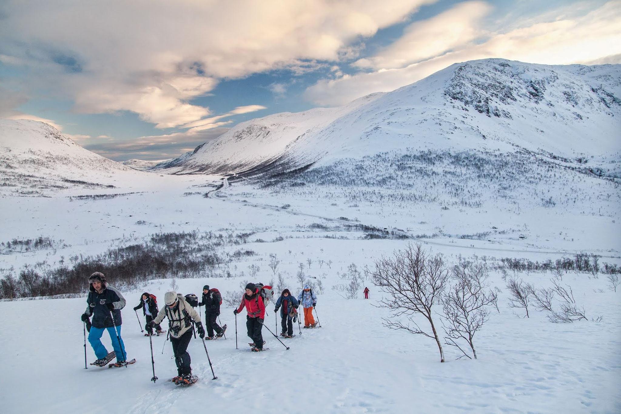 Folk på fottur i snødekte fjell med vinterutstyr.