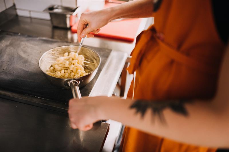 A person wearing an orange apron is stirring a small pot of macaroni and cheese