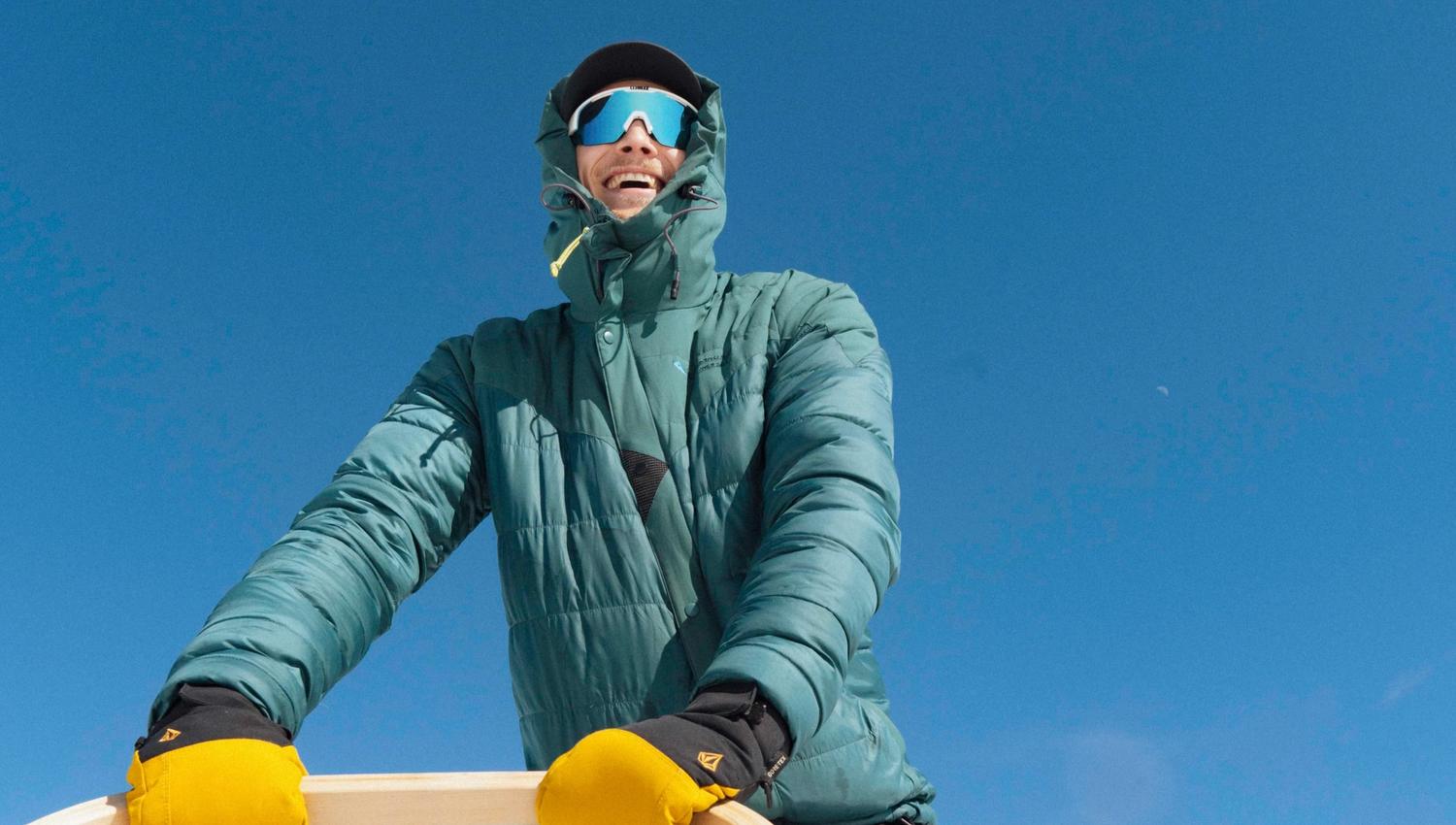 En person kledd i varm jakke og gule hansker står bak et hundespann med huskier på folgefonna husky camp