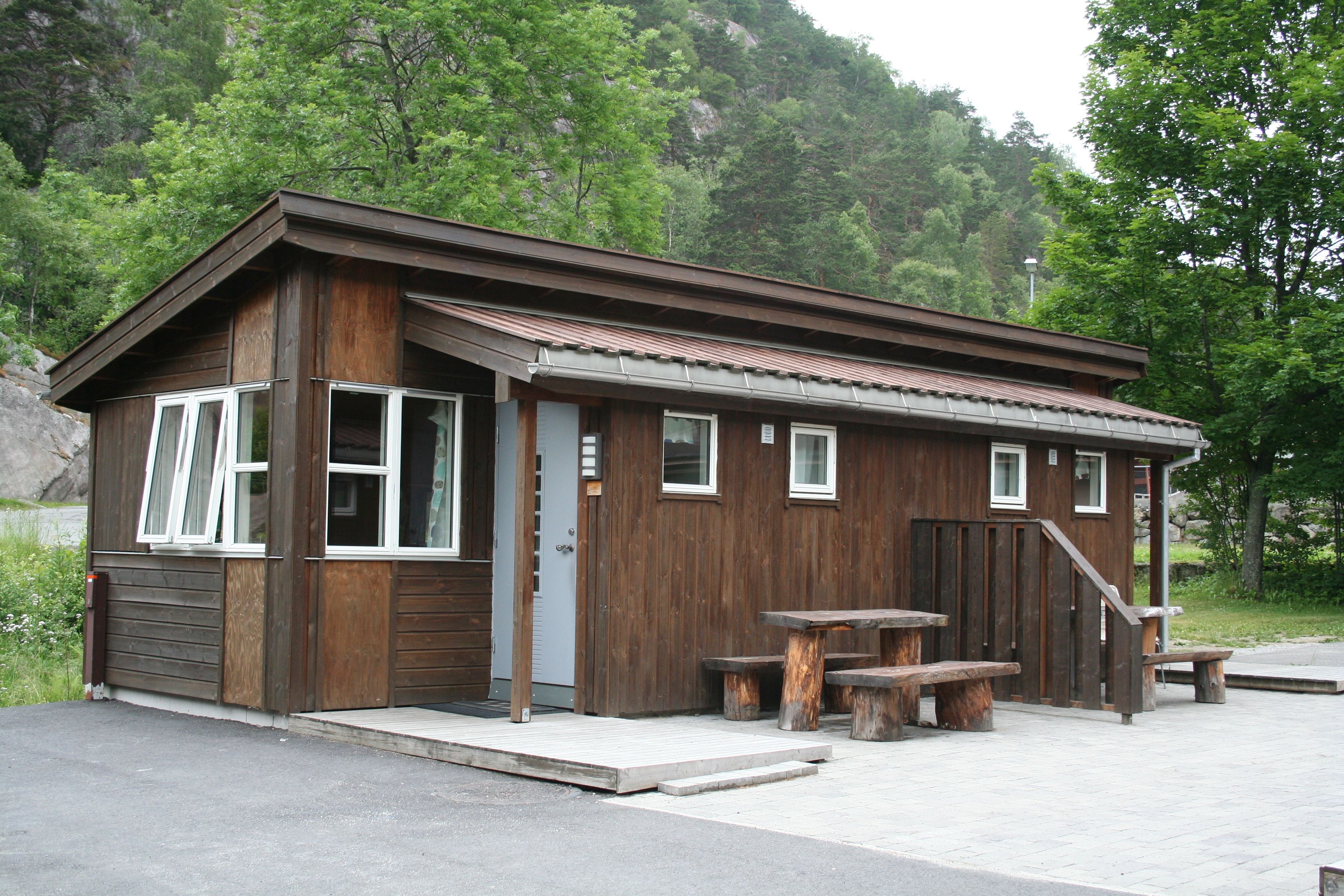 Sanitærbygg i tre ved campingplassen, omgitt av skog og fjell.