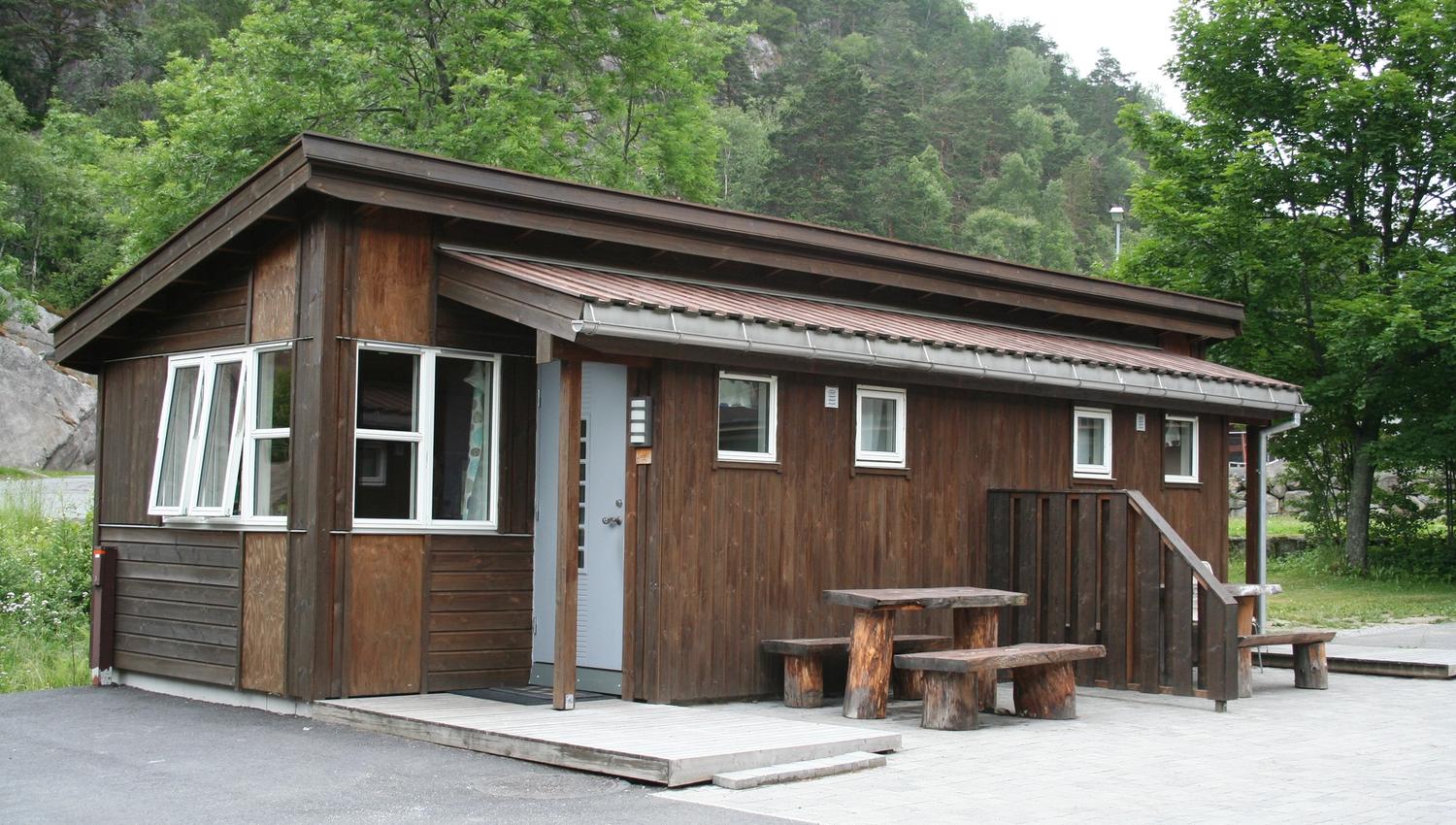 Sanitærbygg i tre ved campingplassen, omgitt av skog og fjell.