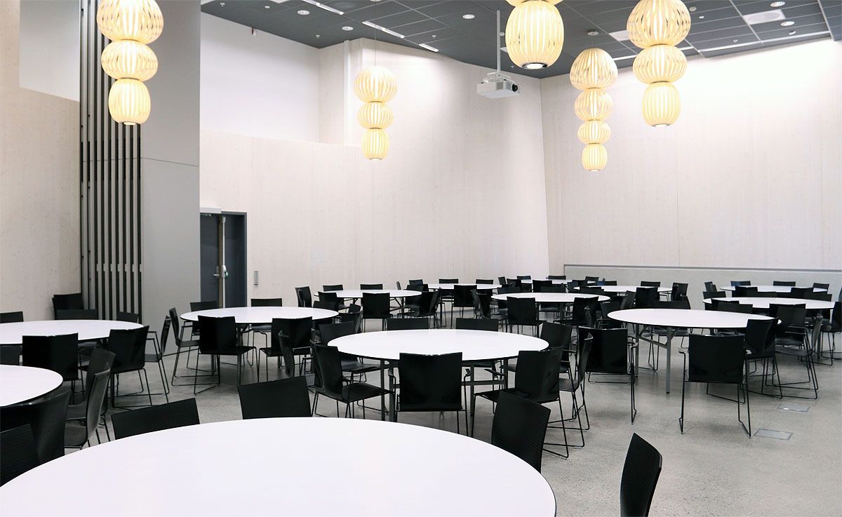 Festsal med store, runde, hvite bord og sorte stoler