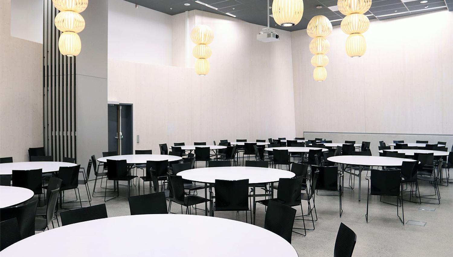 Festsal med store, runde, hvite bord og sorte stoler