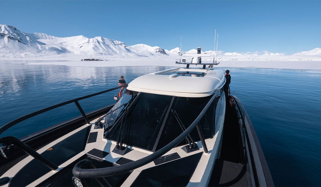 Guests on board MS Kvitbjørn in a fjord with calm blue waters and snow-covered mountains in the background
