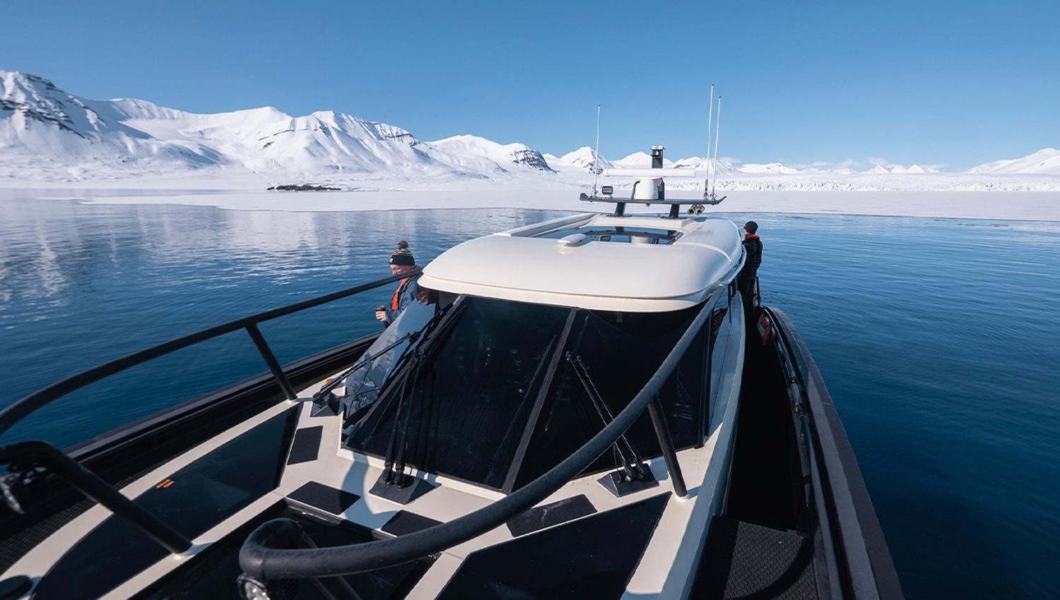 Guests on board MS Kvitbjørn in a fjord with calm blue waters and snow-covered mountains in the background