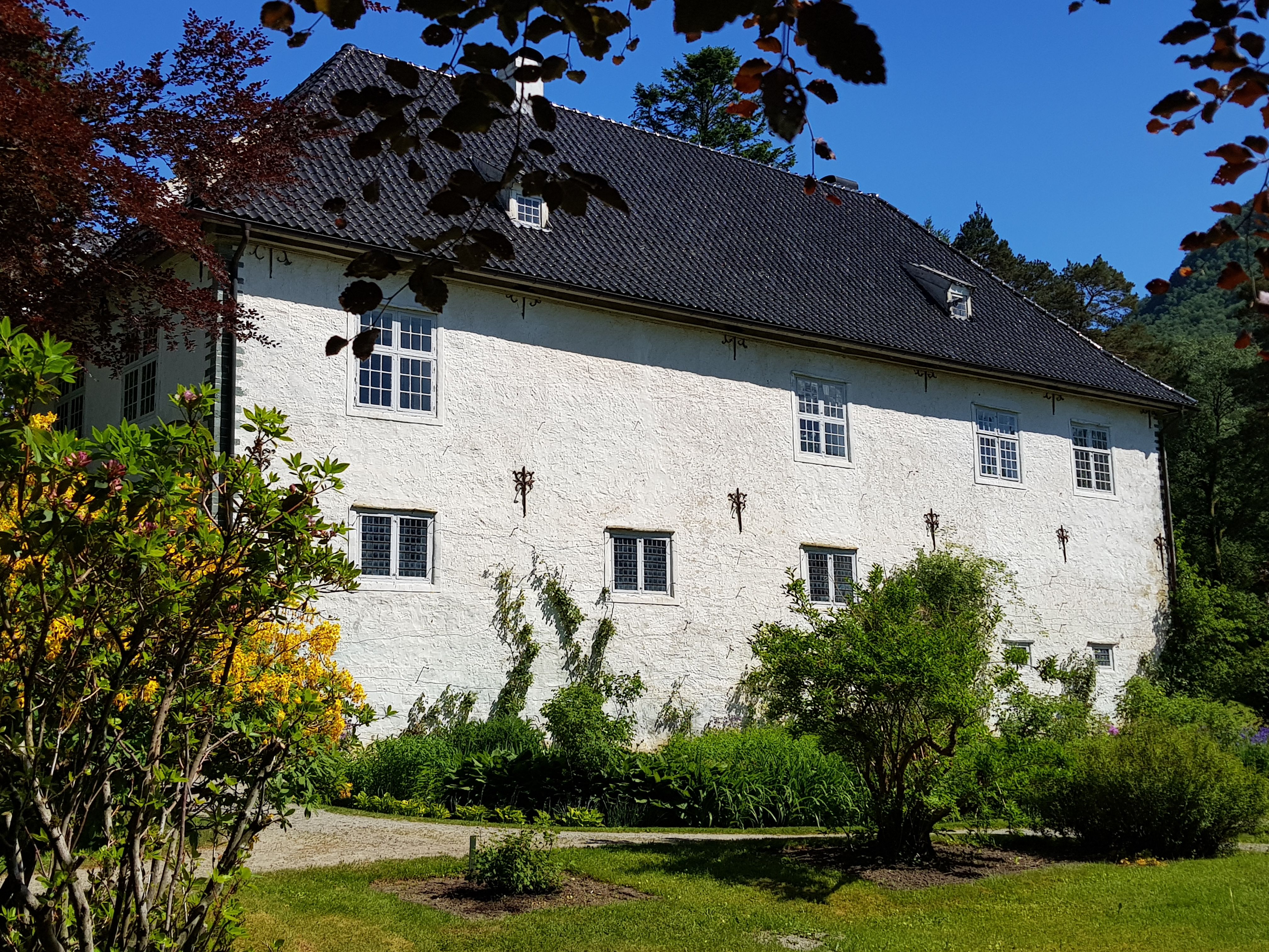 Fasaden på Baroniet Rosendal omgitt av grøn hage og sommarblomar.