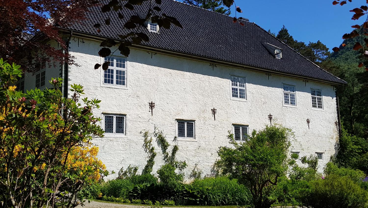 Fasaden på Baroniet Rosendal omgitt av grøn hage og sommarblomar.