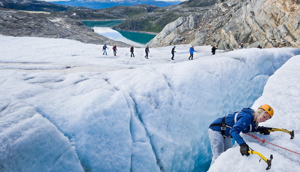 Breførar sikrar ein turdeltakar som klatrar over ei dyp sprekk på Folgefonna-breen.