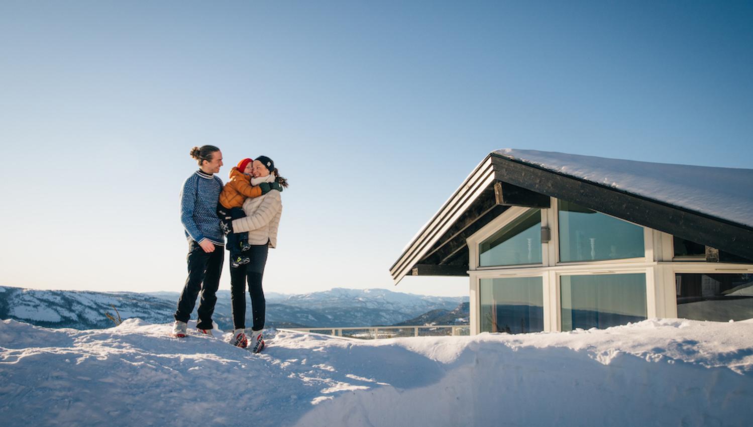 par med barn står foran en hytte på Lifjell Tunet om vinteren
