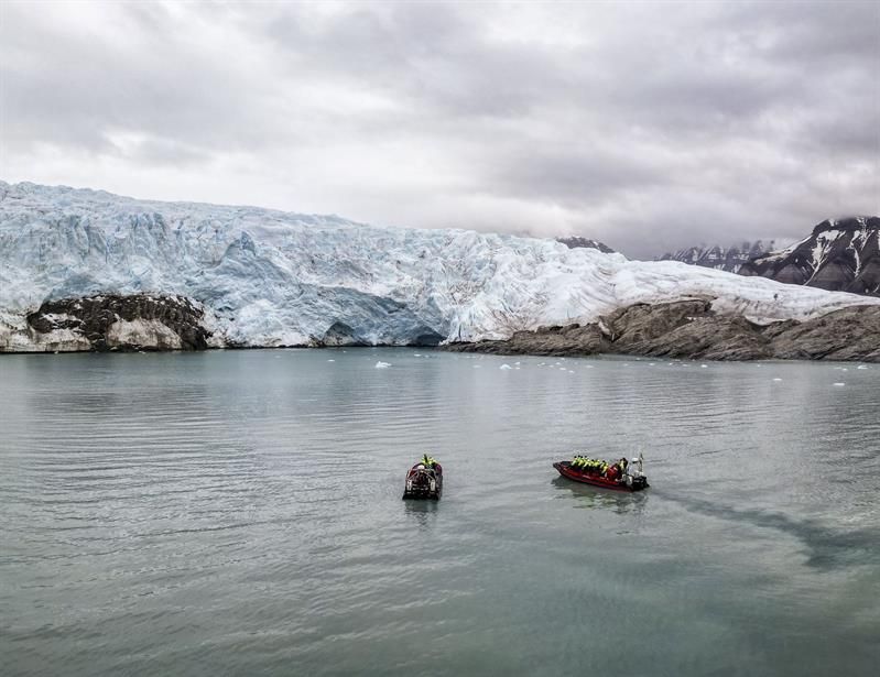 To RIB-båter foran stor isbre i stille fjord.