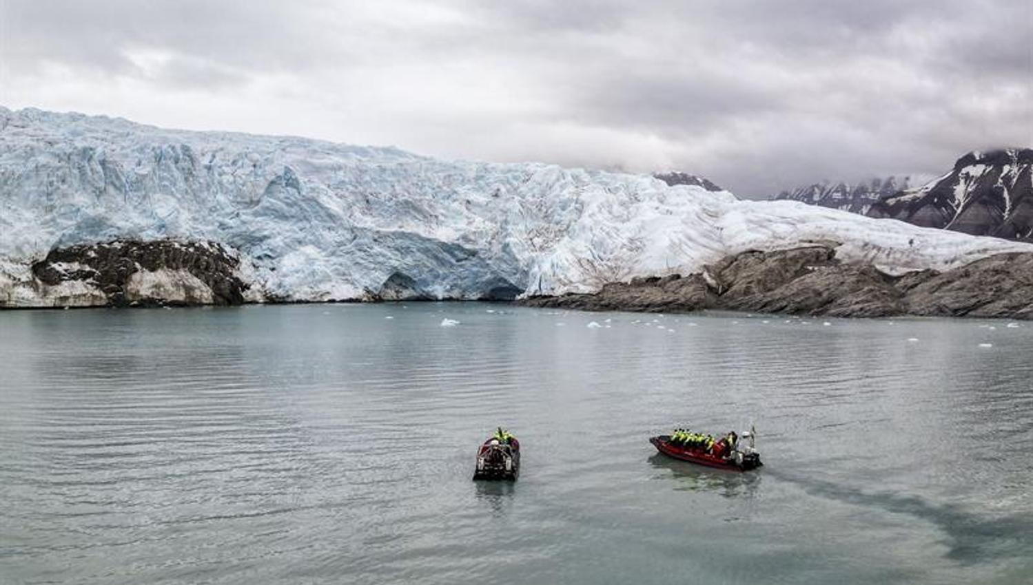 To RIB-båter foran stor isbre i stille fjord.