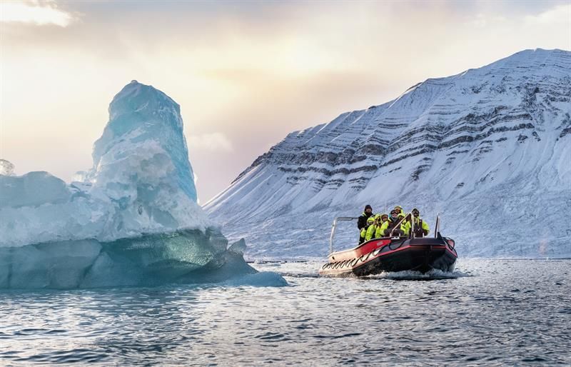 RIB-båt nær stort isfjell i arktisk landskap.