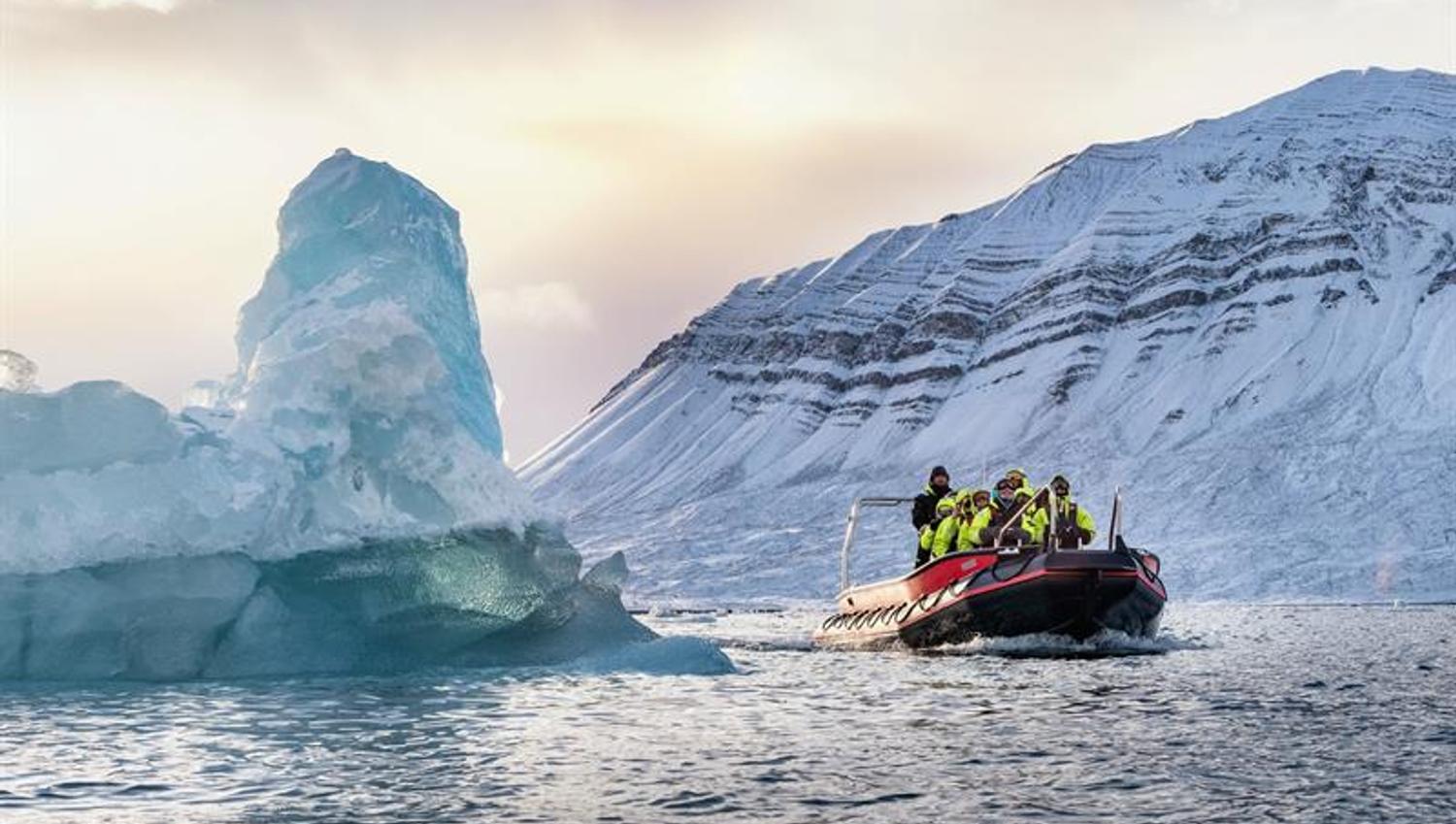 RIB-båt nær stort isfjell i arktisk landskap.
