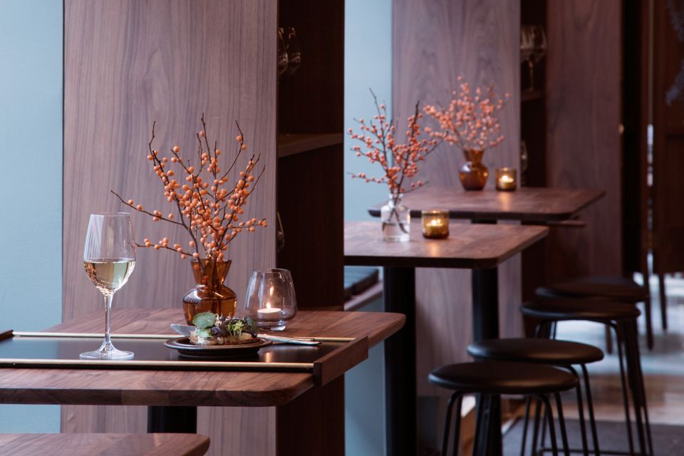 Wooden tables with wine glasses on them, wooden walls and ceiling lamps.