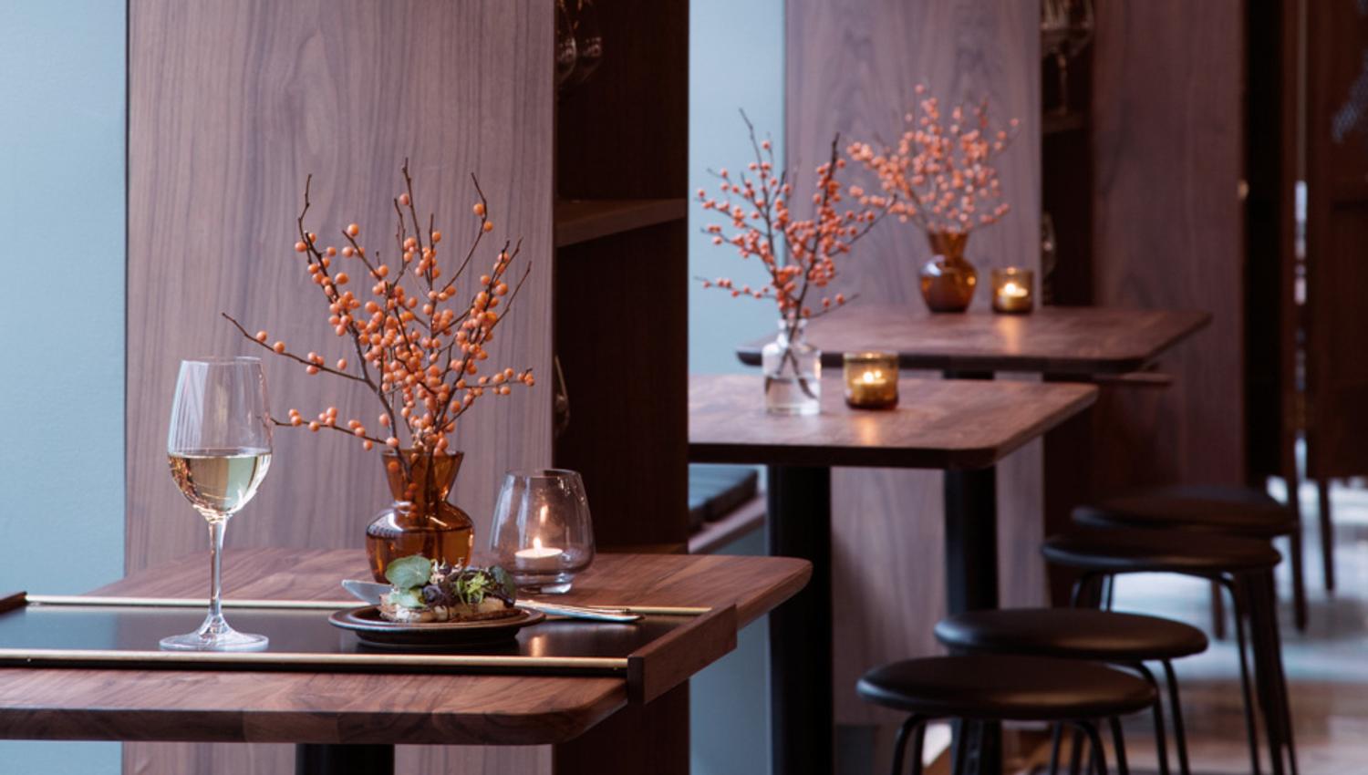 Wooden tables with wine glasses on them, wooden walls and ceiling lamps.