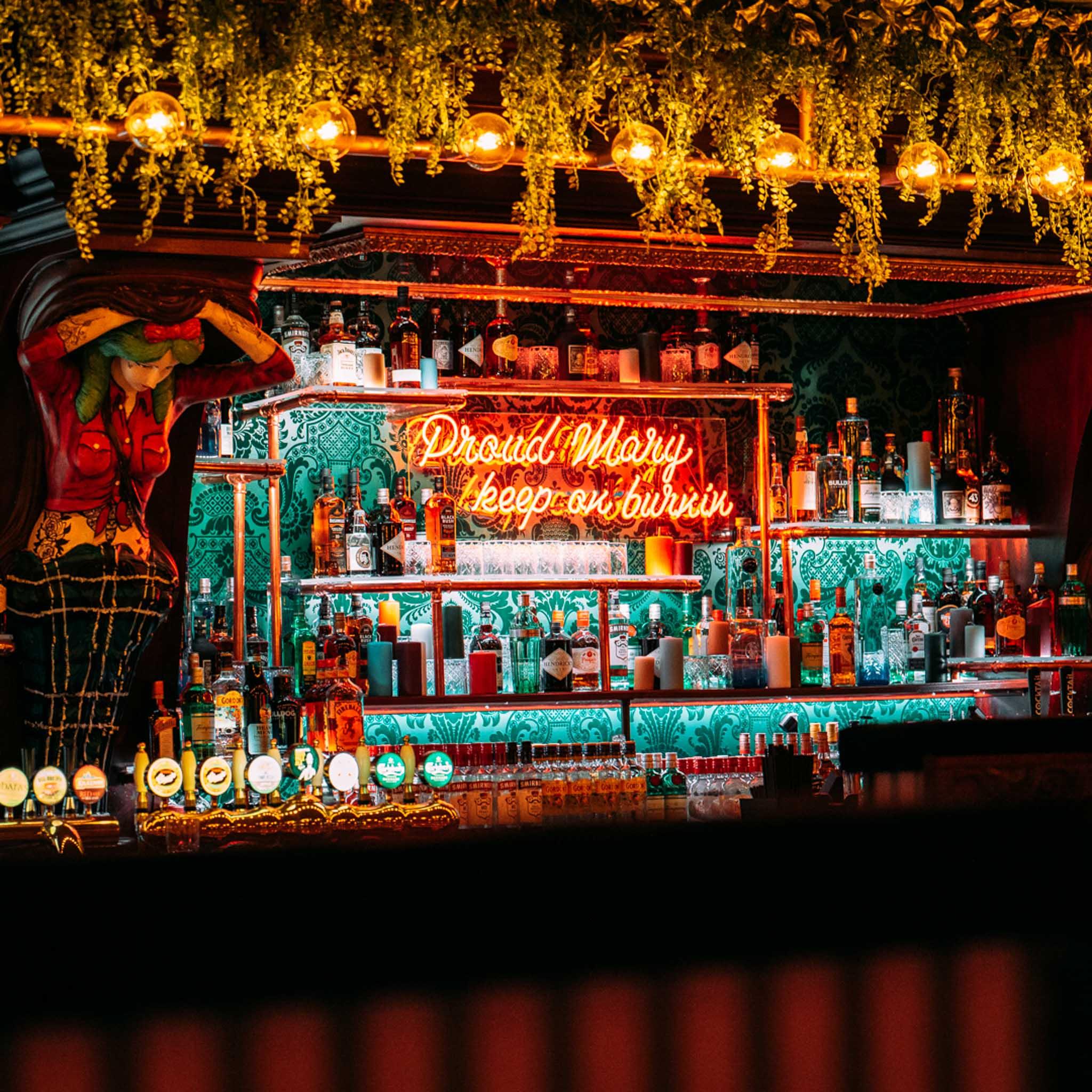 Colourful bar counter with shelved bottles behind it and a neon sign