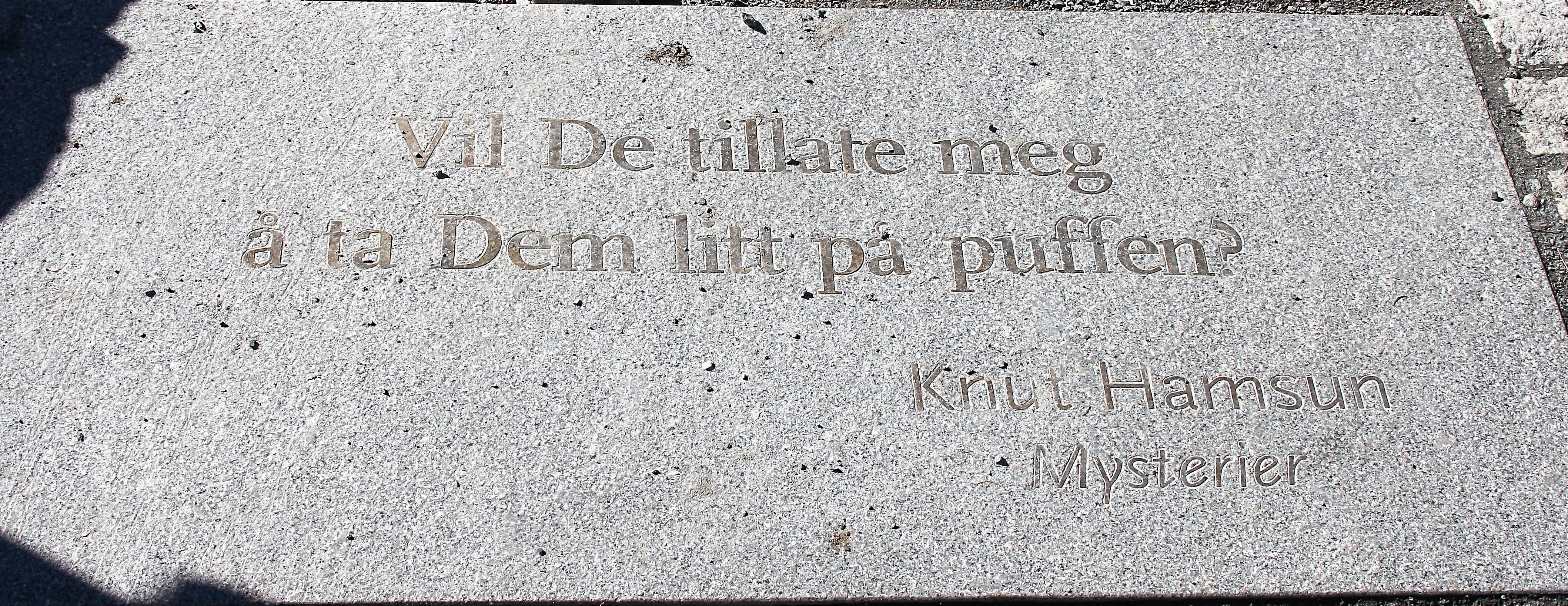Nærbilde av lys granitthelle med innhogd norsk tekst og navnet Knut Hamsun, med sollys og skygger..