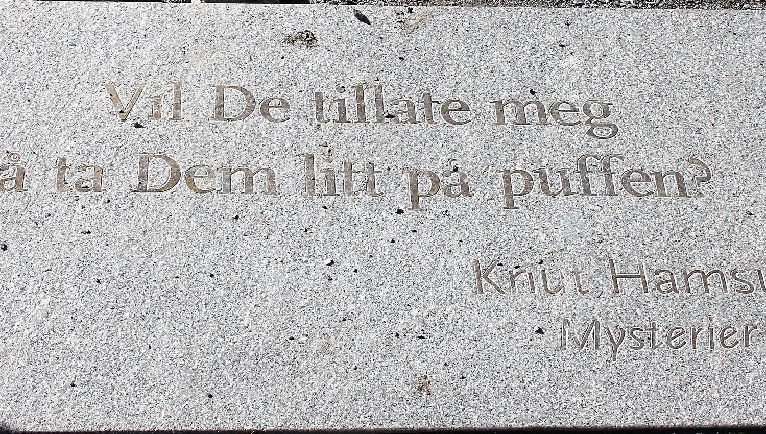 Nærbilde av lys granitthelle med innhogd norsk tekst og navnet Knut Hamsun, med sollys og skygger..