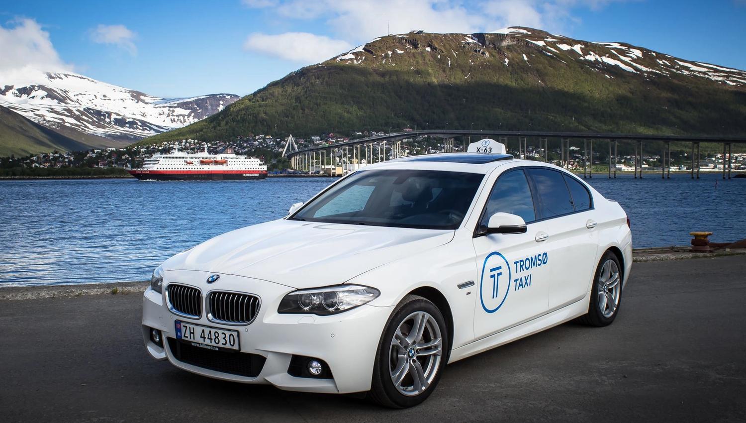 En hvit tromsø taxi bmw med tromsøbruen og hurtigruten i bakgrunnen.
