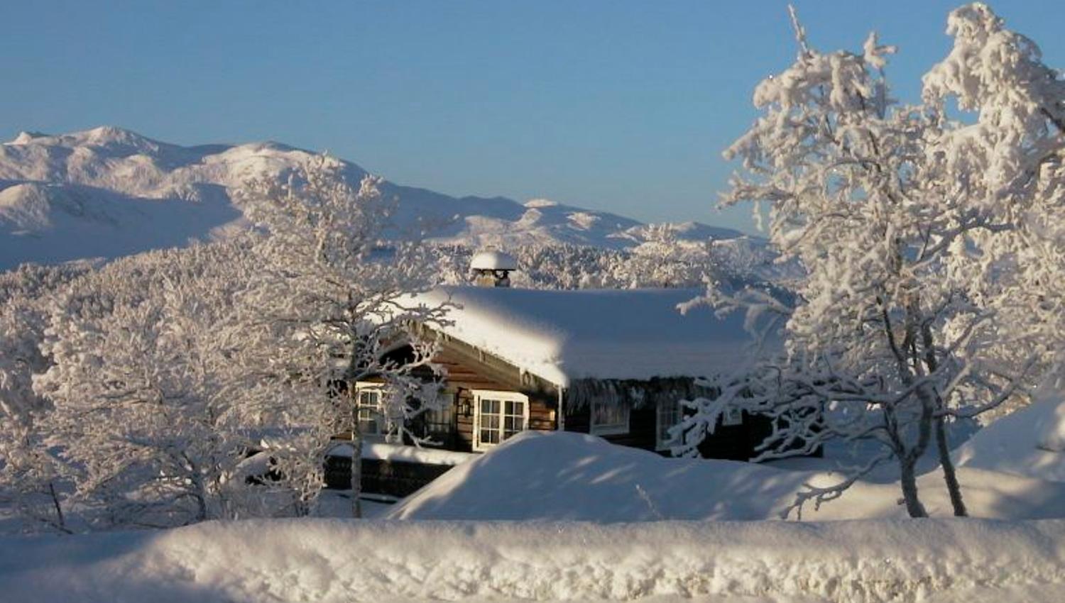 Hytte en vinterdag med snødekte fjell bak.