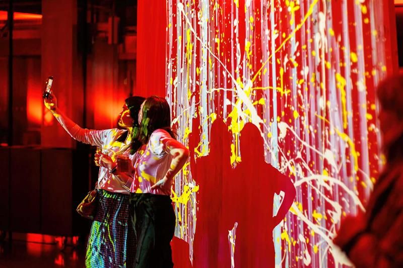 To jenter som tar selfie foran et rødt, abstrakt maleri