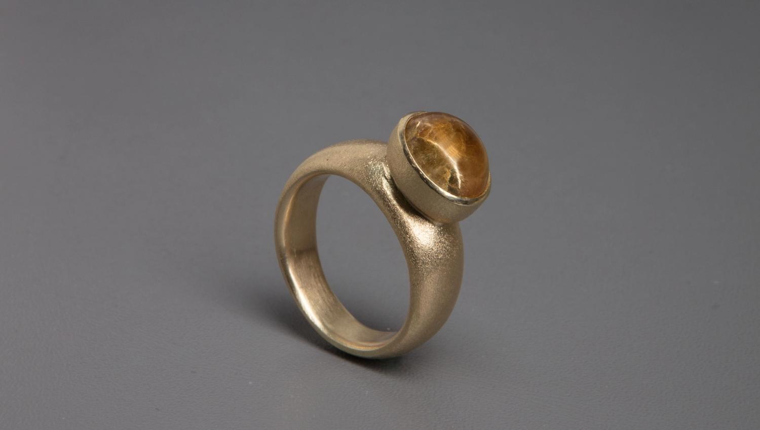 Ring med brun rund edelsten på grå bakgrunn