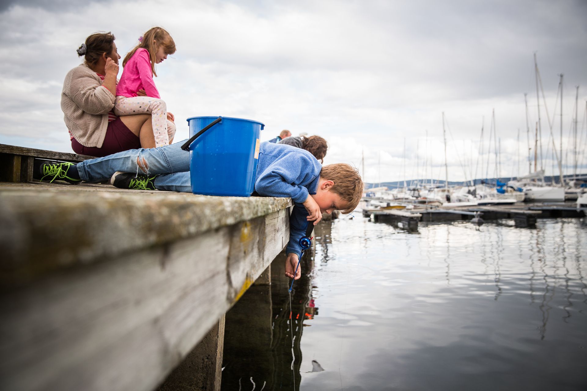 Two kids and an adult on pier, bucket, sea, boats