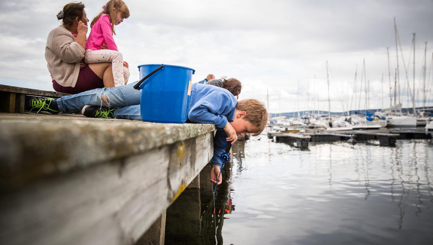 Two kids and an adult on pier, bucket, sea, boats