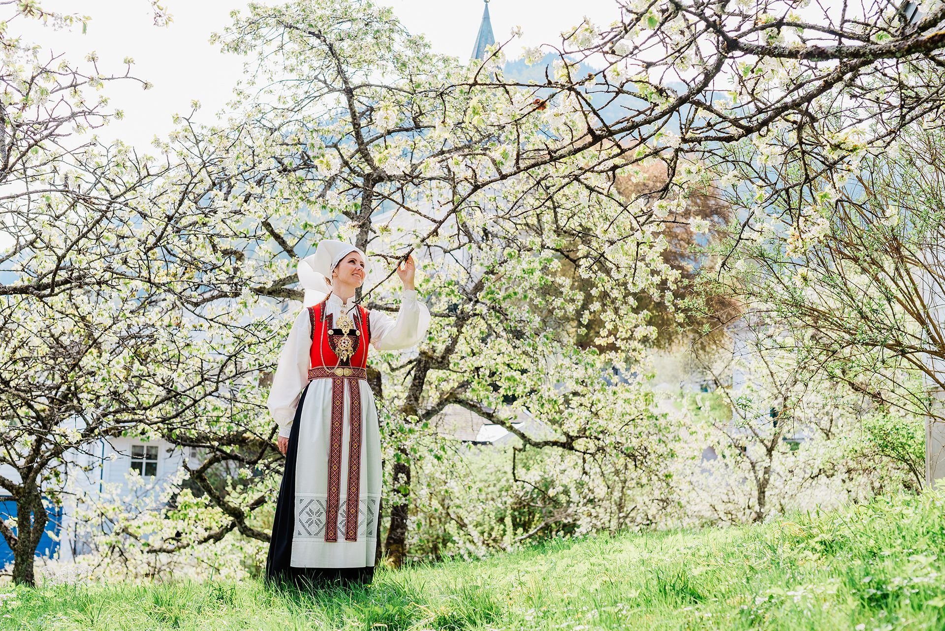 A woman in traditional Norwegian bunad enjoying spring in the idyllic apple orchard at Utne Hotel.