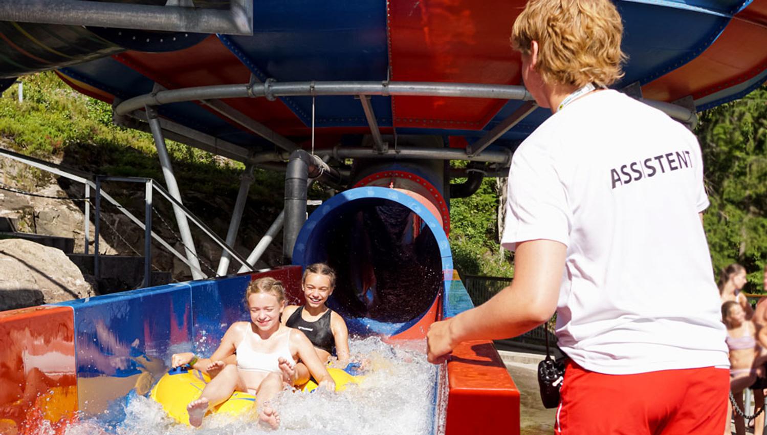 employee from Bø Sommaland assists children at the bottom of a slide
