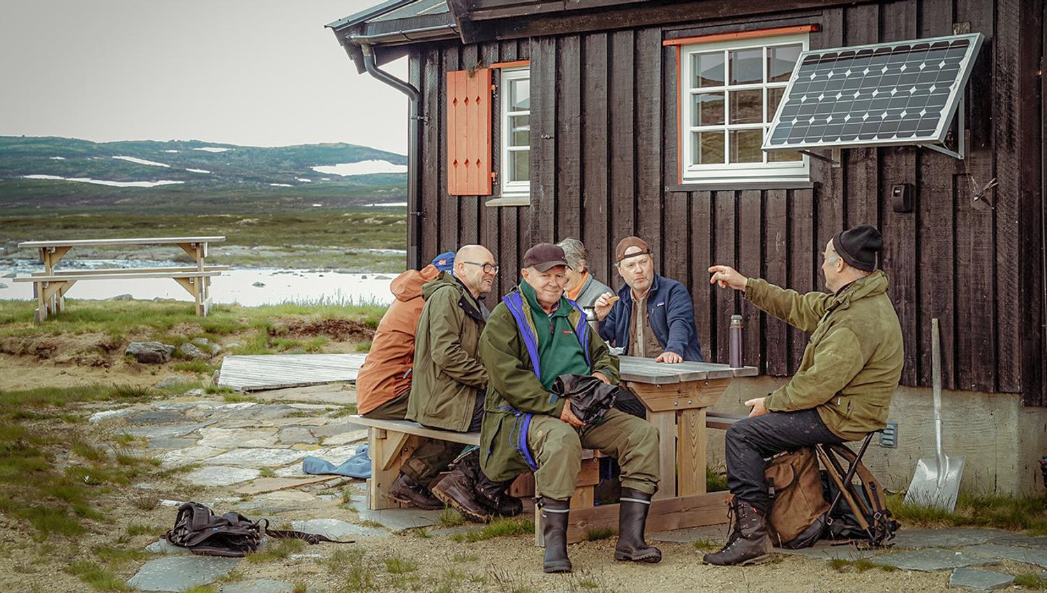 A group of men are sitting around a table, talking and smiling.