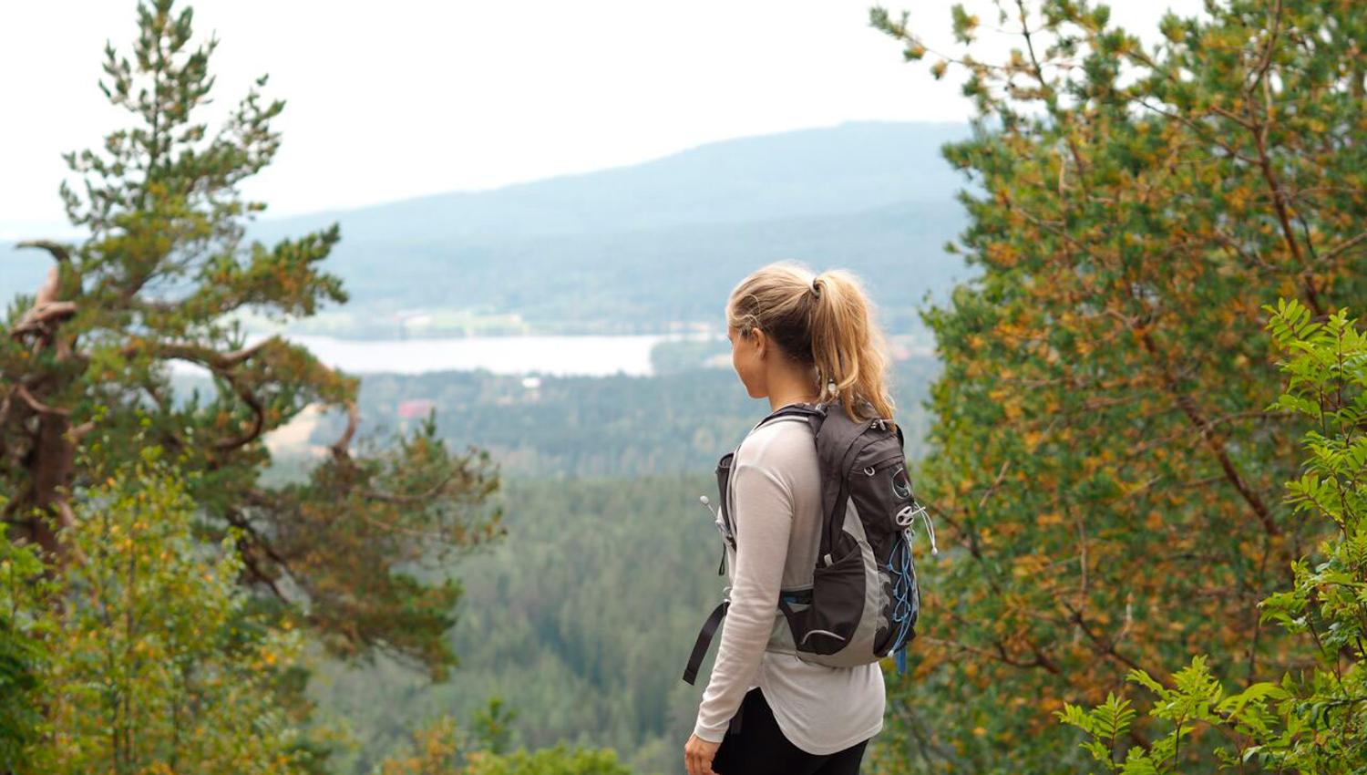 kvinne i skogen med ryggsekk på ryggen