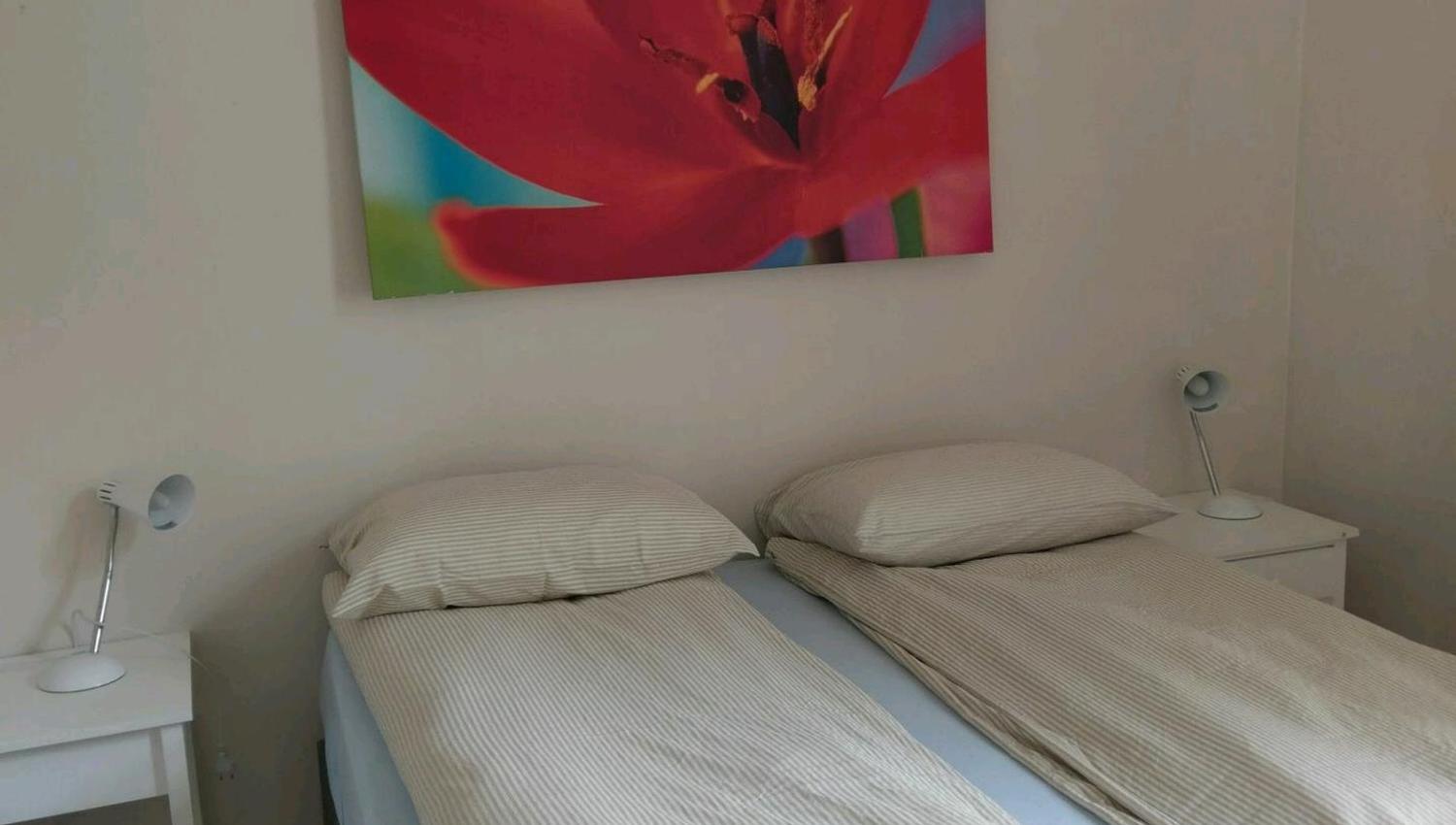 Lyst og komfortabelt soverom på Vikinghaug Apartments med to enkeltsenger og moderne kunst på veggen.
